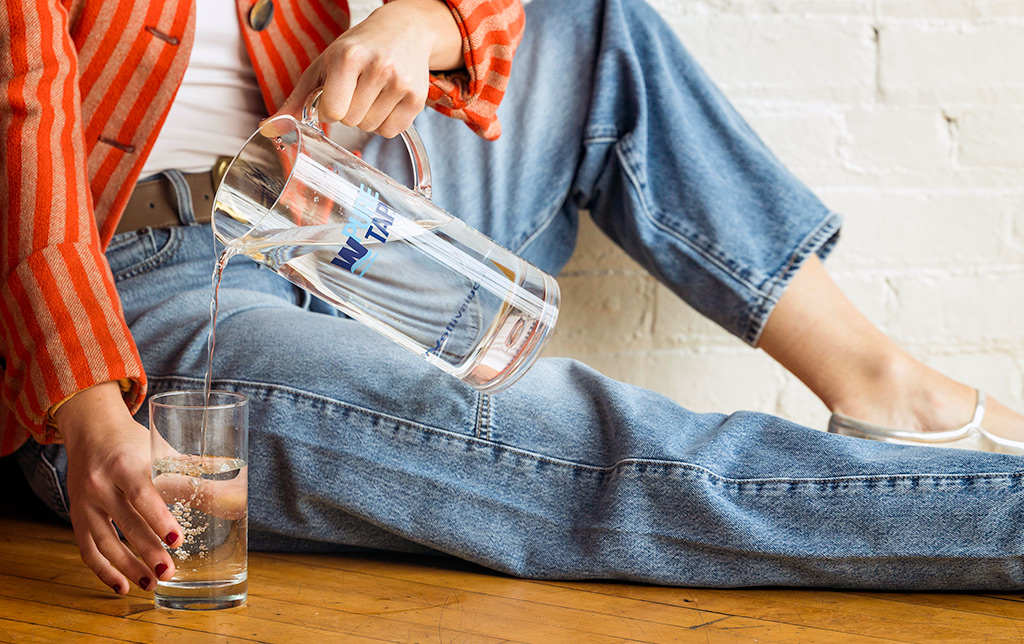 Woman pouring a pitcher of water into glass.